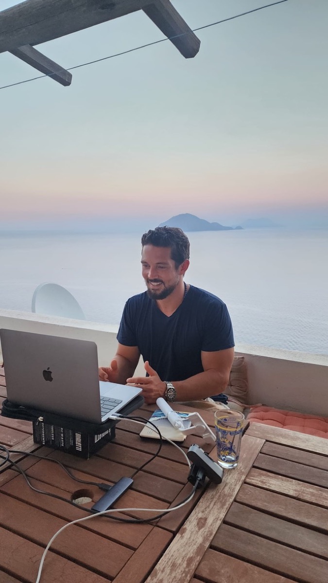 Zach teaching online from a terrace over the sea at dusk